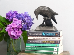 small resin statue of 'Rook With A Book' sat upon a collection flowers Daphne Du Maurier books with a vase of Hydrangeas