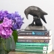 small resin statue of 'Rook With A Book' sat upon a collection flowers Daphne Du Maurier books with a vase of Hydrangeas