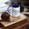 Two tone white and navy blue mug with Thrussells blue bird with coffee and cake