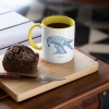 Two tone white and yellow mug with Thrussells blue bird with coffee and cake